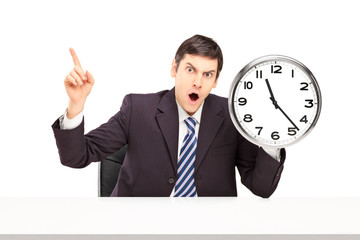 Angry businessman sitting and holding a wall clock