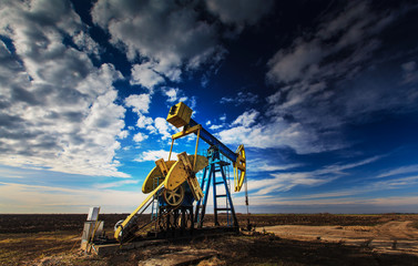 Operating oil well profiled on dramatic cloudy sky