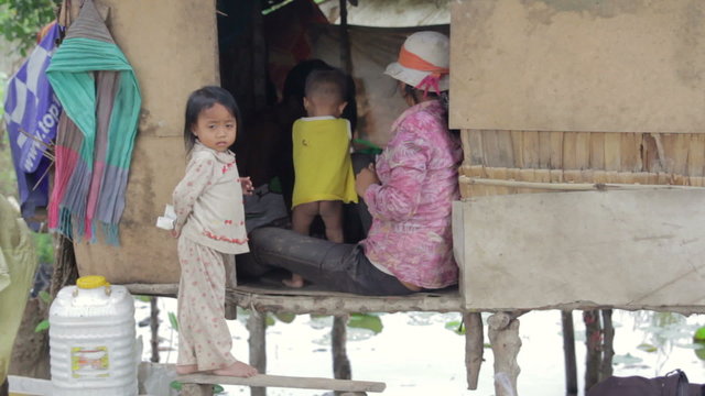 Cambodian kid holding money in slum, shacks at background