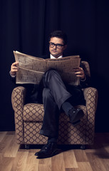 Man with cigarette and newspaper sitting in vintage armchair