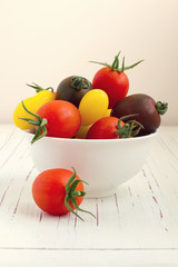 Assorted tomatoes in white bowl on bright background
