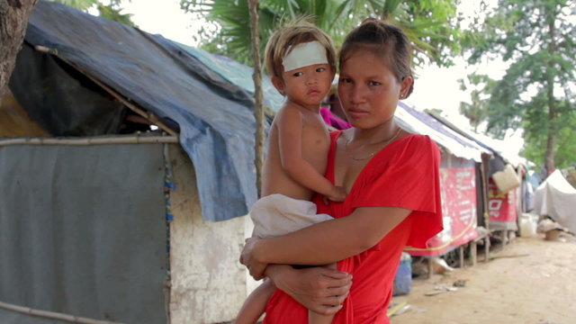 Mother holding baby in cambodian shanty, close dumping area