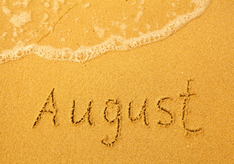 August - written in sand on beach texture