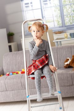 Cute little girl sitting on ladder at home