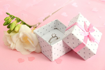 Beautiful box with wedding ring and flower on pink background