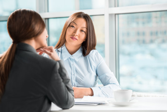 Two business women talking and signing contract at office