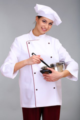 Portrait of young woman chef with pan on grey background