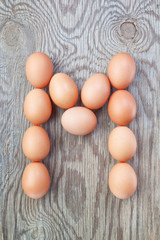 A letter m from the eggs for Easter. On a wooden texture.