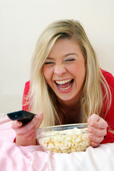 Joven mujer comiendo palomitas de maíz y viendo televisión.