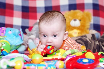 Fototapeta na wymiar Dziecko leżące wśród zabawek gryzie grzechotkę