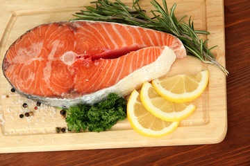 Fresh salmon steak on cutting board, on wooden background