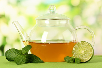 Teapot with mint and lime on table on bright background