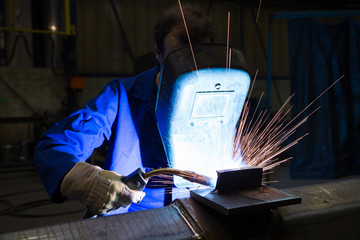 Worker with welding helmet welds steel