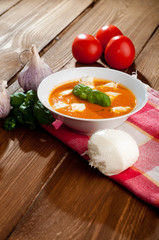 Tomato soup with shredded cheese in ceramic bowl on a wooden tab