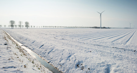 Fototapeta na wymiar Wind turbine in a snowy field in sunlight
