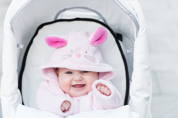 Laughing baby girl in white stroller in bunny dress-up