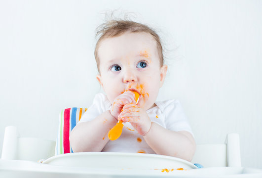 Sweet messy baby eating a carrot in a white high chair
