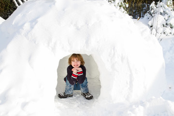 Funny boy playing in a snow igloo