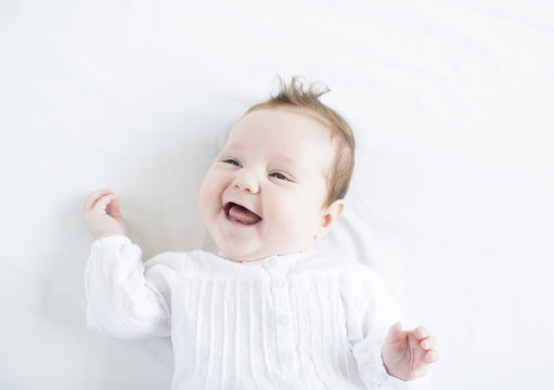 Adorable baby girl in a white dress laughing