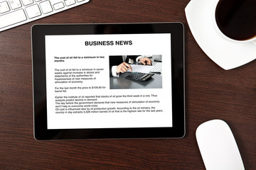 Computer tablet is on the table with business news on screen