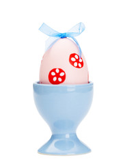 Pink colored easter egg is in blue egg cup, isolated