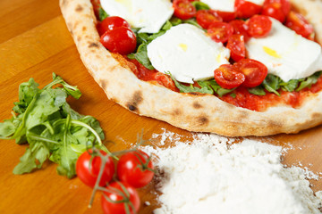 Typical Italian Pizza, ingredients in background on wood table