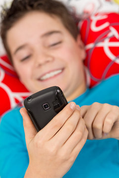 Junge liegt entspannt mit Handy / Smartphone im Bett