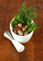 Herbs and spices in ceramic mortar, on wooden background