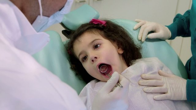 Dentist and assistant, checking teeth of young baby girl