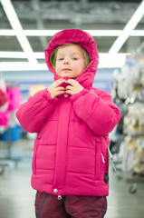 Adorable girl fitting winter jacket and hat in sport store