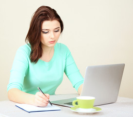 Beautiful young woman working on laptop on light background