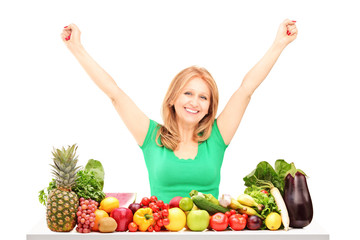 Happy woman with raised hands posing with pile of fruits and veg