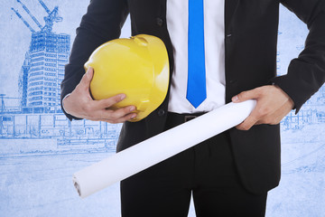 Businessman holds safety helmet and blueprint