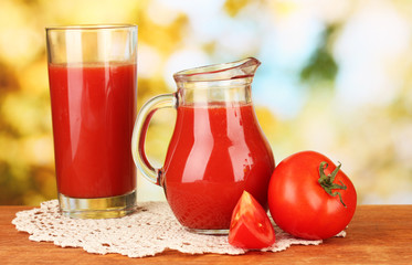 Full jug of tomato juice, on wooden table on bright background