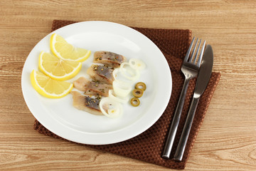 Dish of herring and lemon on plate on wooden table close-up