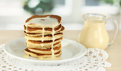 Sweet pancakes on plate with condensed milk on table in kitchen