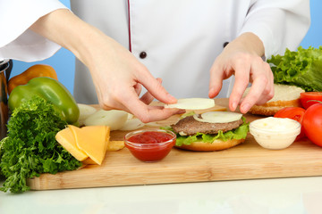 Female hands preparing cheeseburger, on blue background