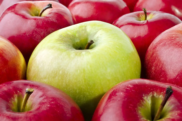 Green apple surrounded by red apples close-up