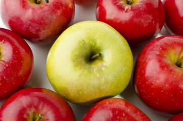 Green apple surrounded by red apples close-up