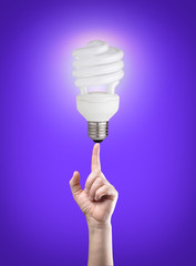 Energy saving light bulb on tip of finger.Purple background