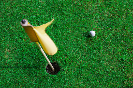 A golf ball and a hole with yellow flag