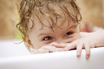 Playful baby hiding in bath and smiling