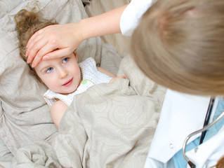 Top view of sick child lying in bed and visiting her doctor