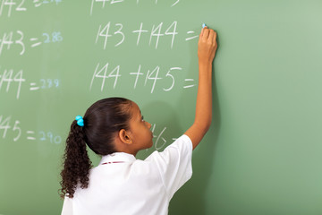 primary school girl writing maths answer on chalkboard