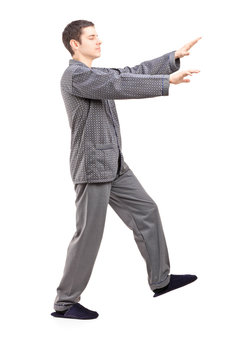 Full length portrait of a young man in pajamas sleepwalking
