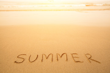 Summer - text written by hand in sand on a beach.