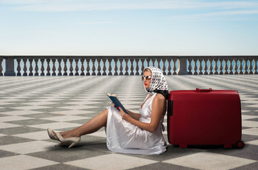 Retro woman with sunglasses and suitcase reading book portrait 