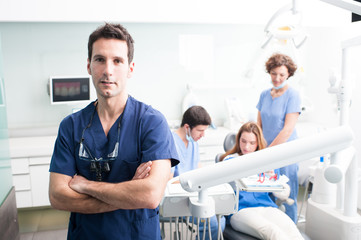 A portrait of a dentist with his team working in the background