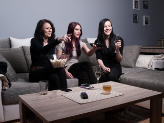 three women watch television and eat popcorn