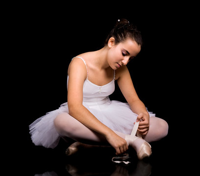 Ballerina putting her ballet shoe against black background.